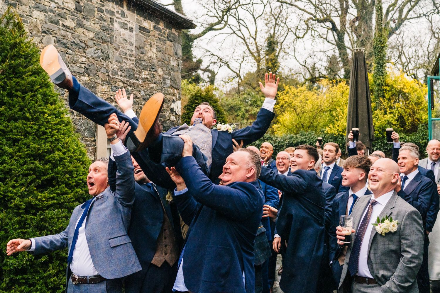 Groomsmen lift and toss someone in the air during outdoor wedding celebrations.  Virginia Park Lodge Wedding Photographer Cavan Dublin Irela