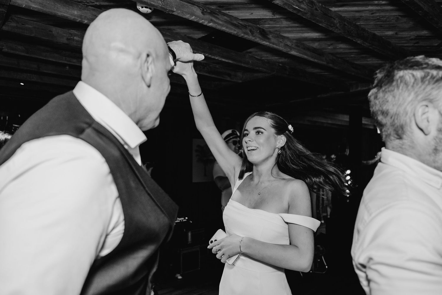 Black and white photo of wedding guests dancing and celebrating at a dimly lit reception. The Dean Dublin Wedding Photographer