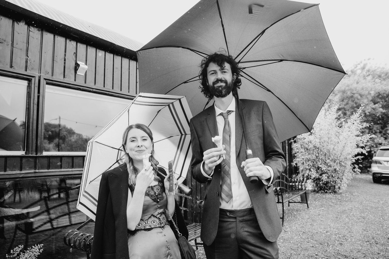 Couple sharing an umbrella and laughing together in a black and white outdoor portrait. Wedding photographer Dublin