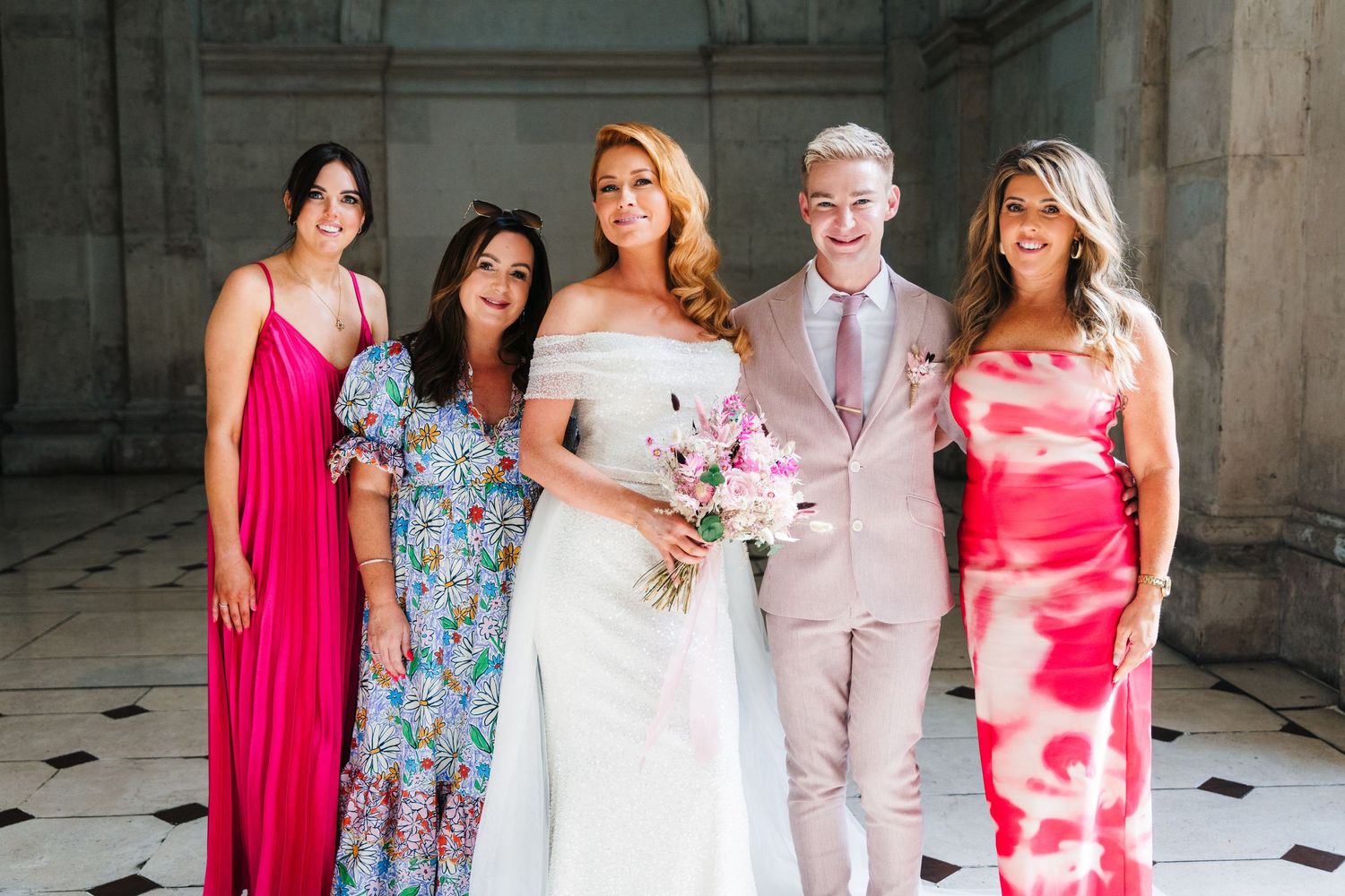 Wedding party in pink and floral dresses standing together on a tiled floor.  city hall dublin wedding photos