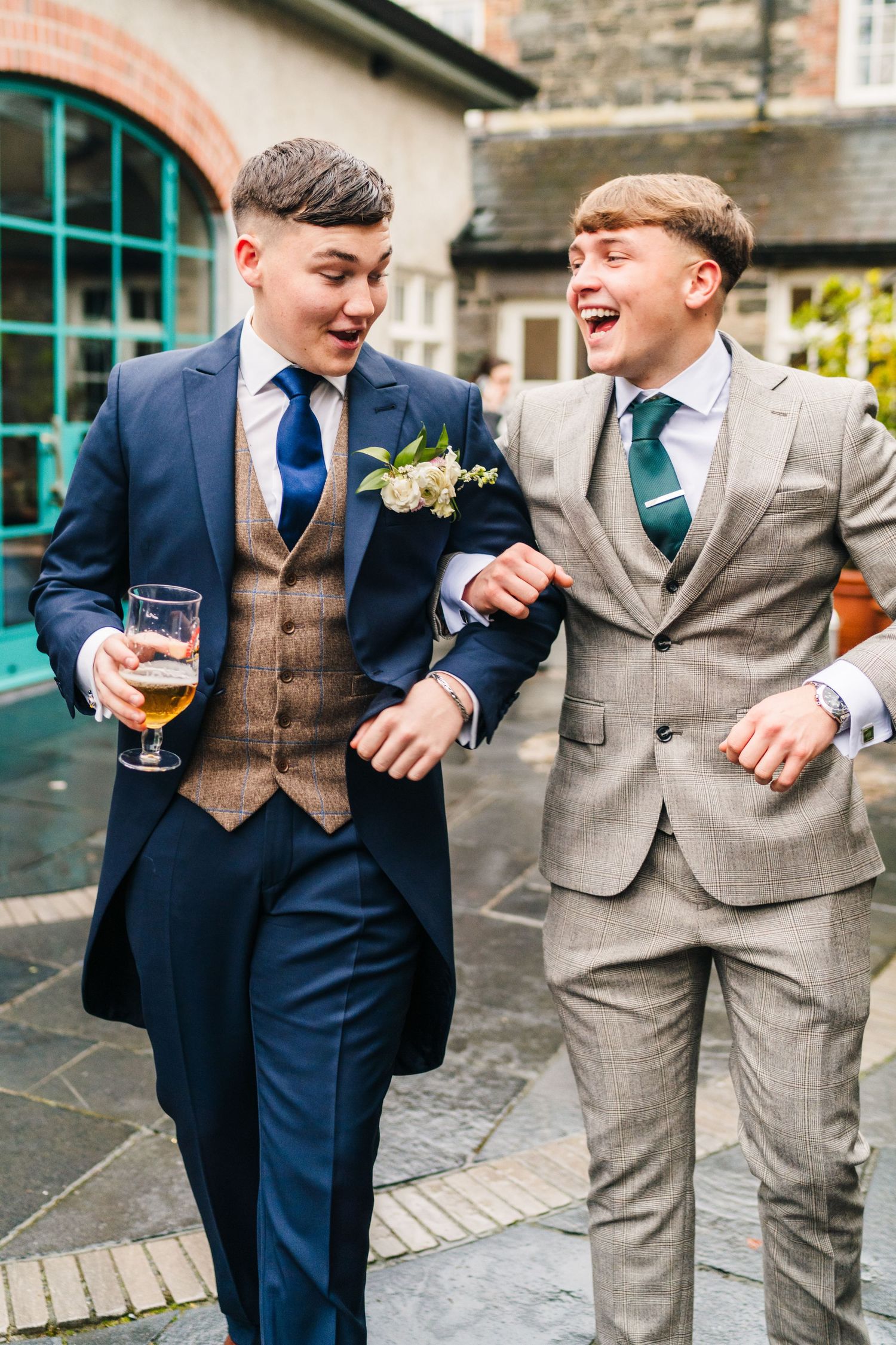 Two groomsmen in tailored suits share a laugh while holding drinks at an outdoor wedding venue.  Virginia Park Lodge Wedding Photographer Ca