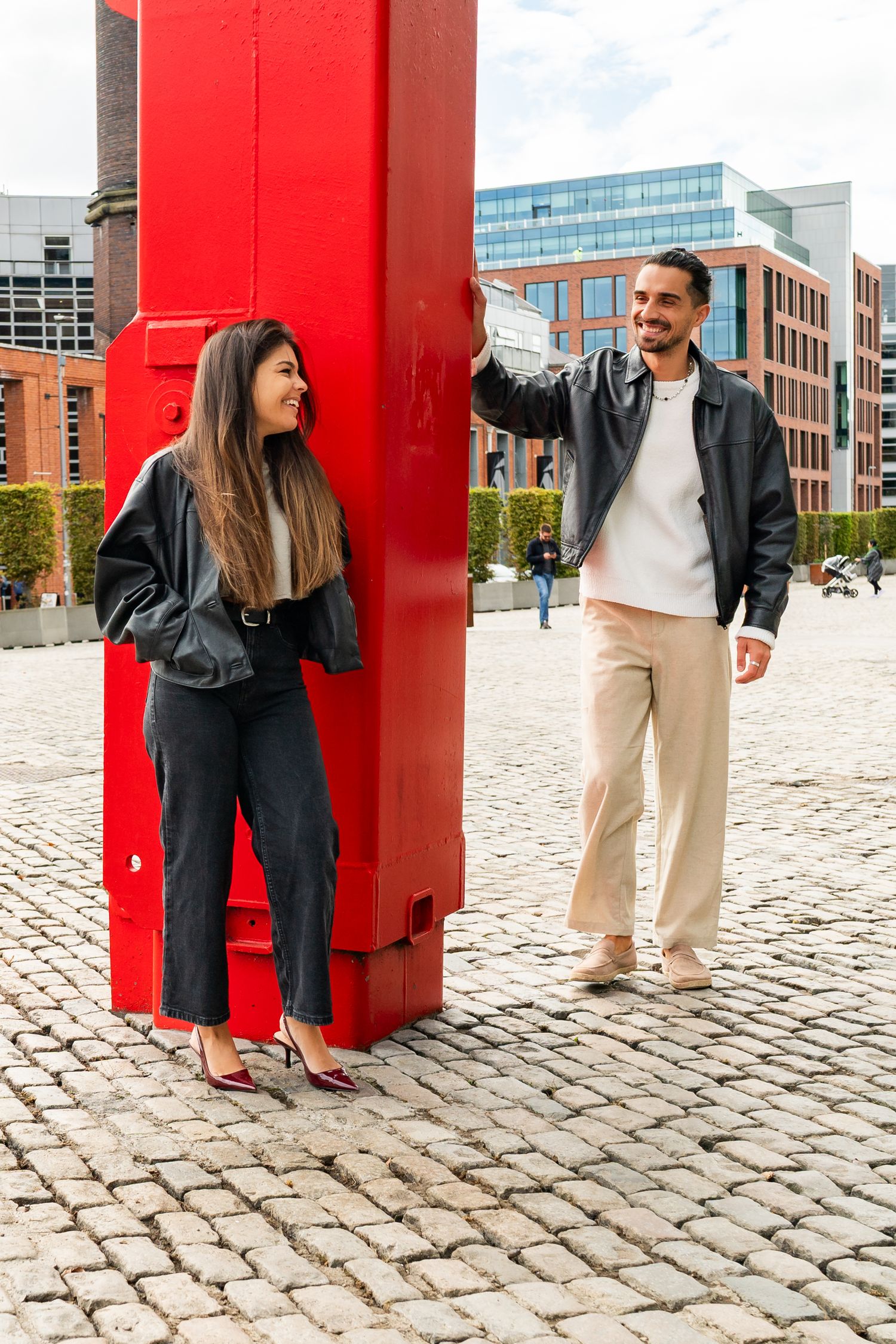 A couple poses creatively around a bright red architectural column on cobblestone ground. Couple's Photoshoot PHOTOGRAPHER Dublin