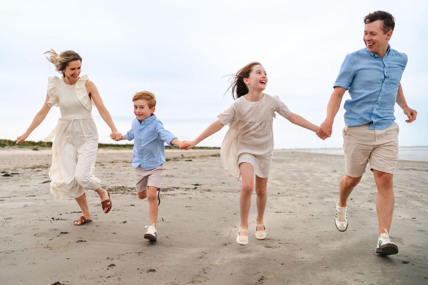 Family of four holding hands and running together on a beach.  Family photographer Dublin Ireland