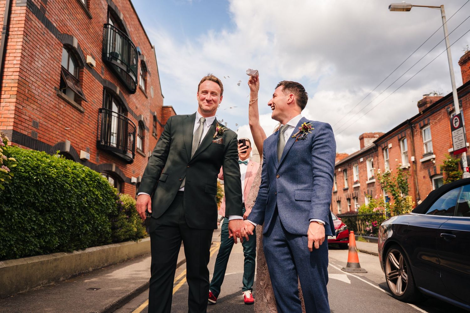 Wedding party walking and laughing on a residential street with red brick houses. Same sex wedding PHOTOGRAPHER Dublin