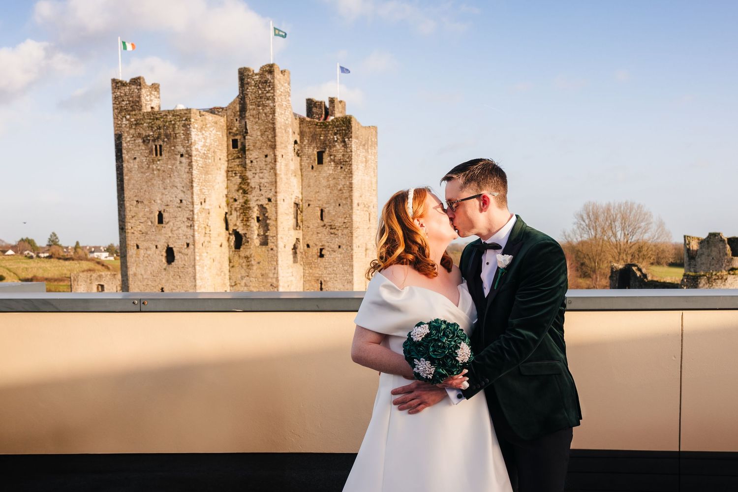 A couple shares a romantic moment on their wedding day with a historic medieval castle tower in the background.  Wedding PHOTOGRAPHER Trim C