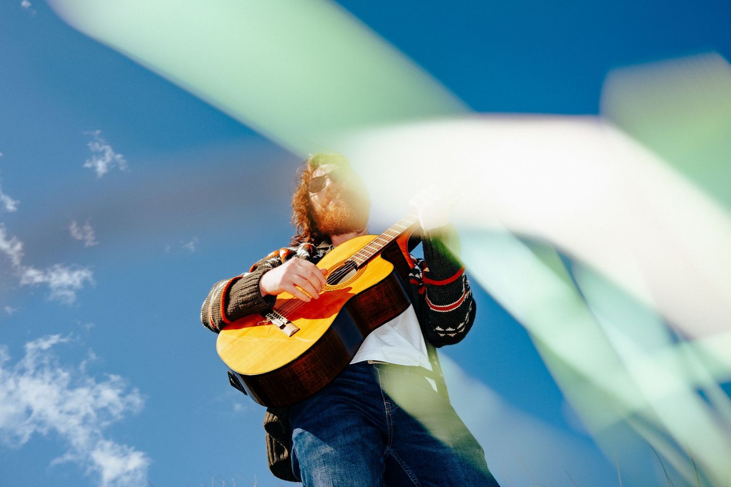 Person playing acoustic guitar against blue sky with propeller blades in soft focus. PHOTOGRAPHER Dublin