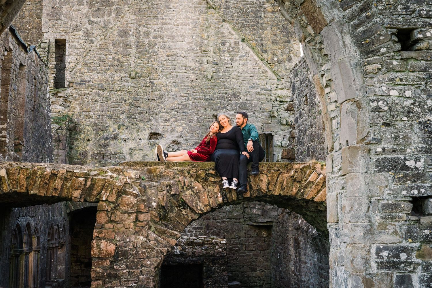 A couple poses playfully on a stone bridge inside historic castle ruins. Family PHOTOGRAPHER Dublin