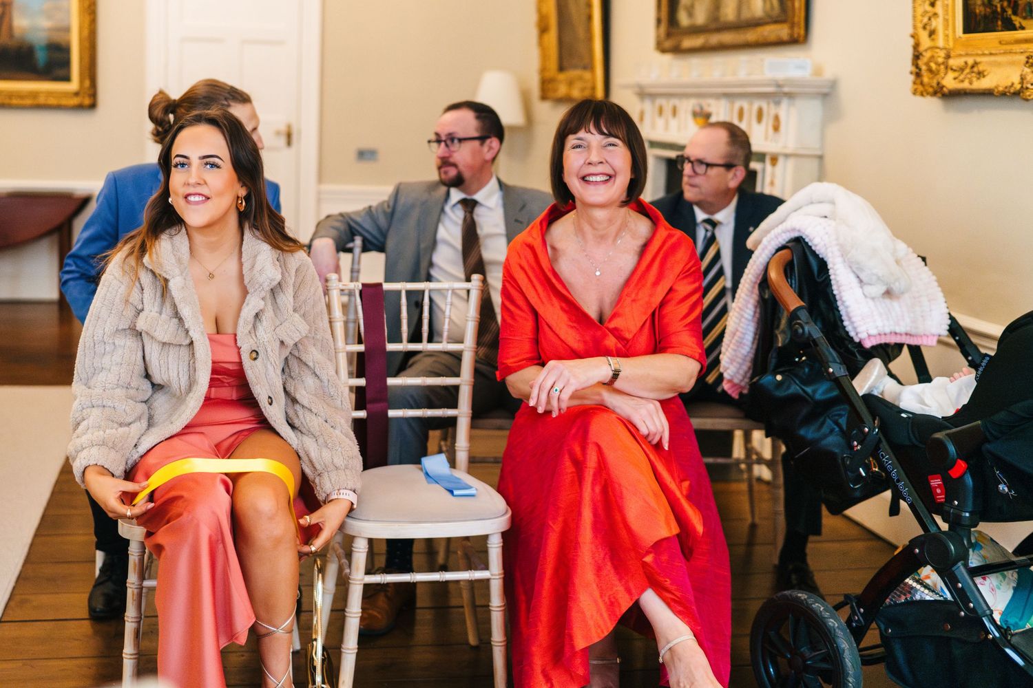 Wedding party celebrating indoors with bridesmaids in red dresses and elegant decor in the background.  Wedding PHOTOGRAPHER Dublin