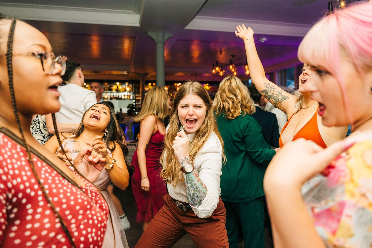 Energetic wedding guests dancing and celebrating at a lively reception with purple lighting. PHOTOGRAPHER Dublin Ireland Wedding