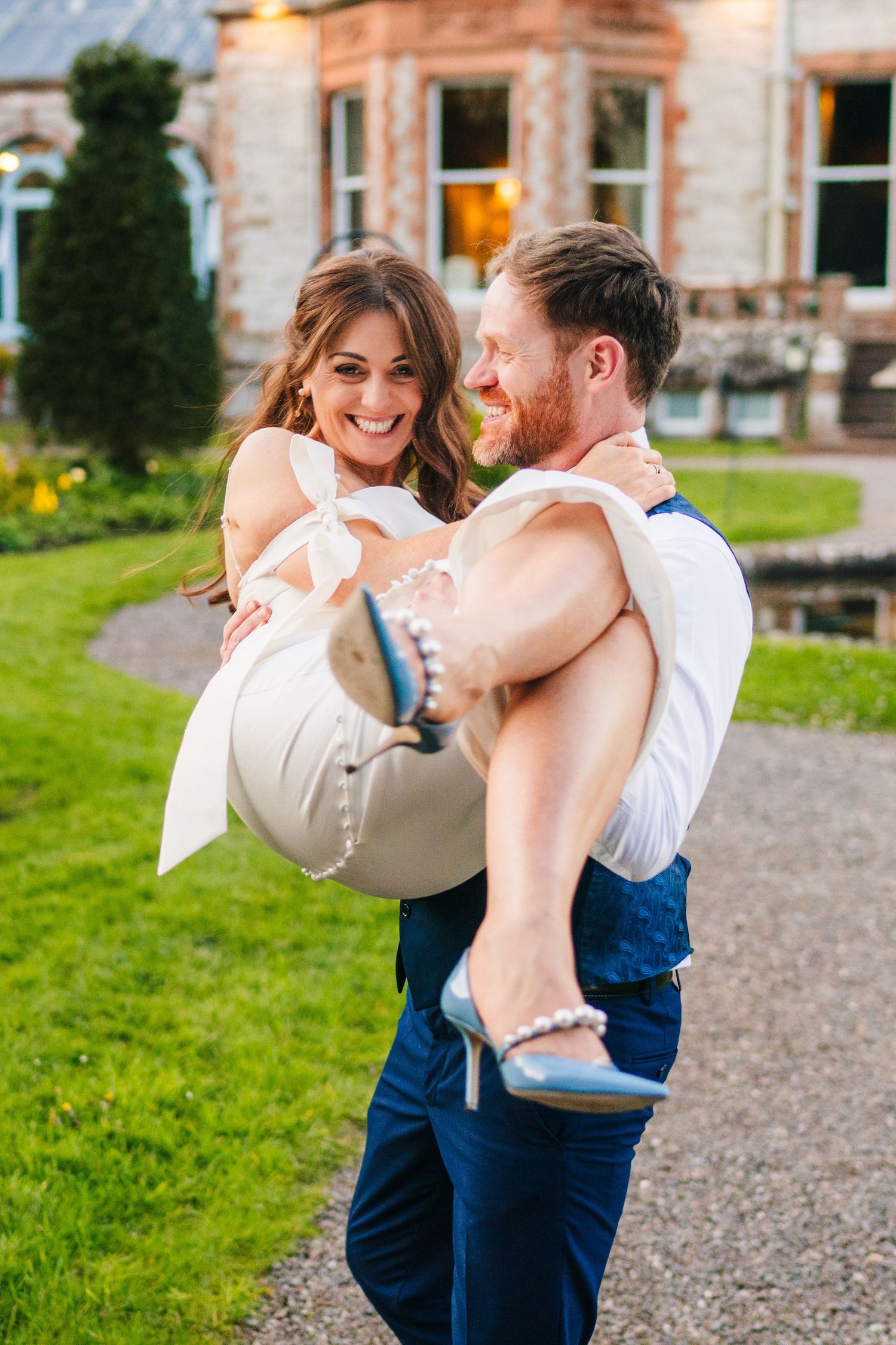 Castle Leslie Wedding PhotograpA couple shares a joyful moment together on the lawn of a beautiful stone manor house with blooming gardens.