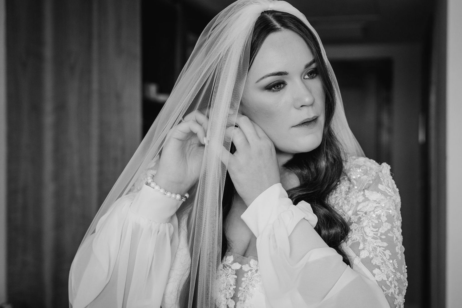 Bride wearing an elegant white wedding dress with embellished lace details and delicate veil against dark background. Portmarnock Hotel Wedd