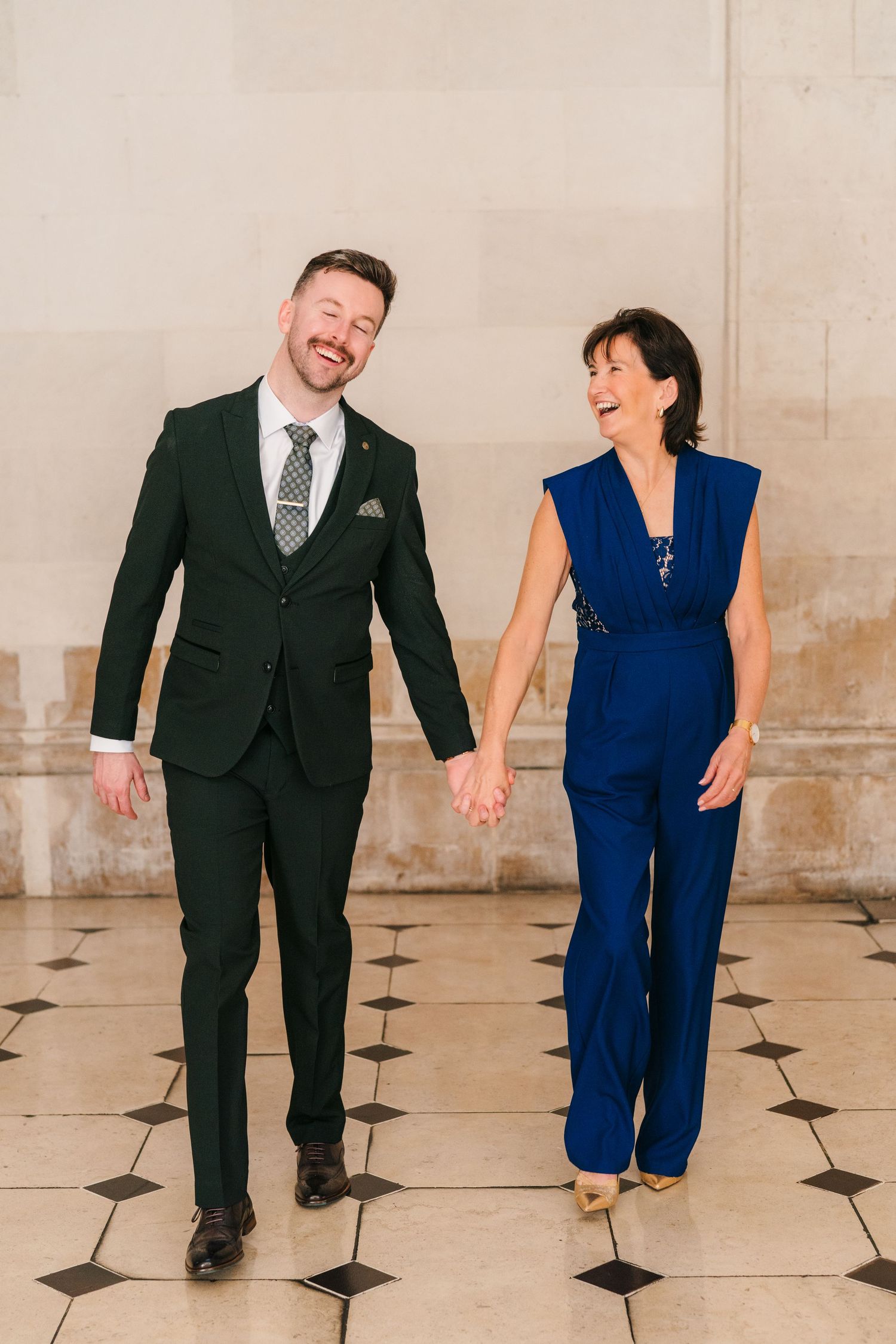Couple in contrasting formal wear laughs while walking on checkered floor. City Hall Dublin wedding photogrAPher