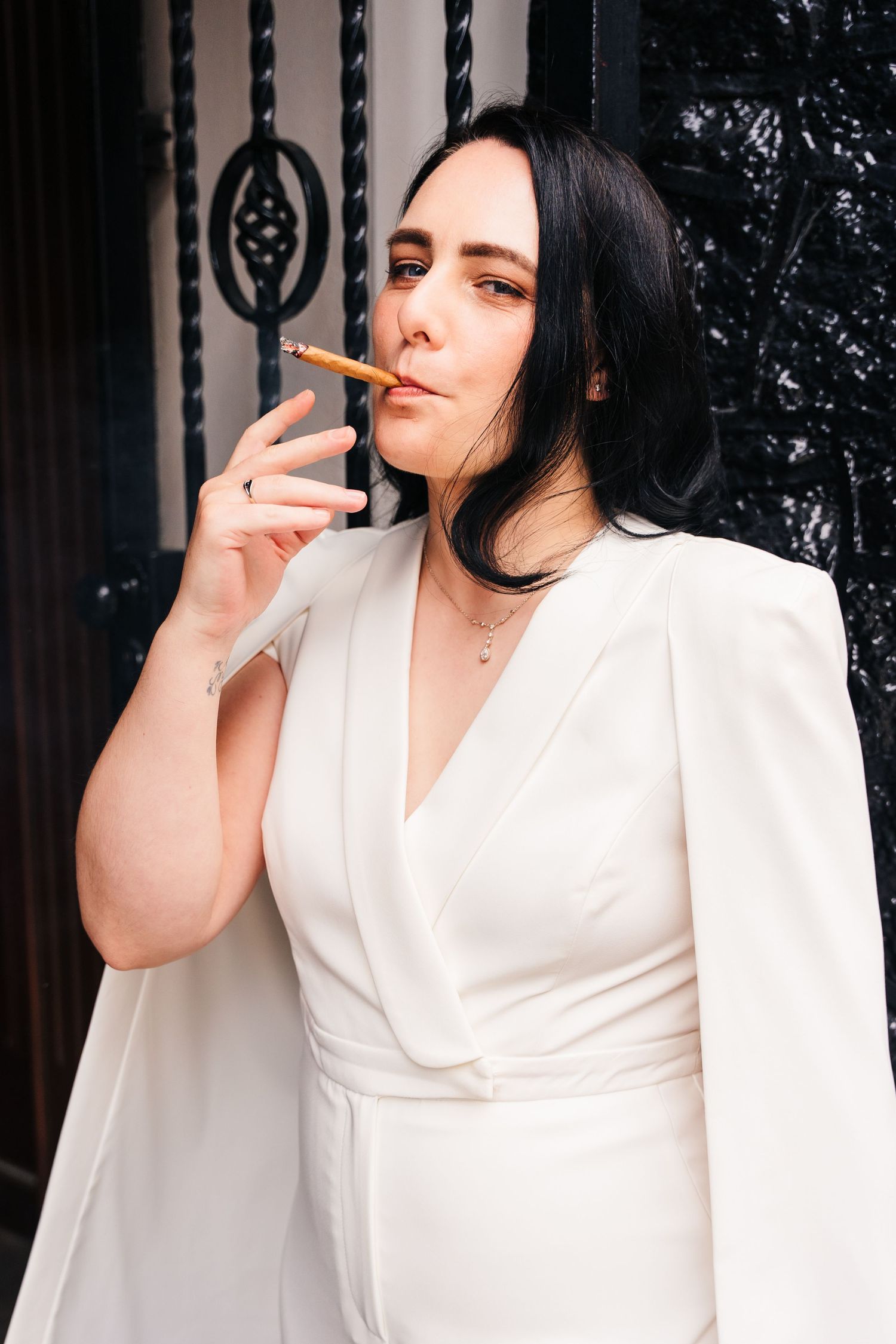A person in a white wrap dress poses against a dark background while smoking a cigar. House Dublin Wedding Photographer