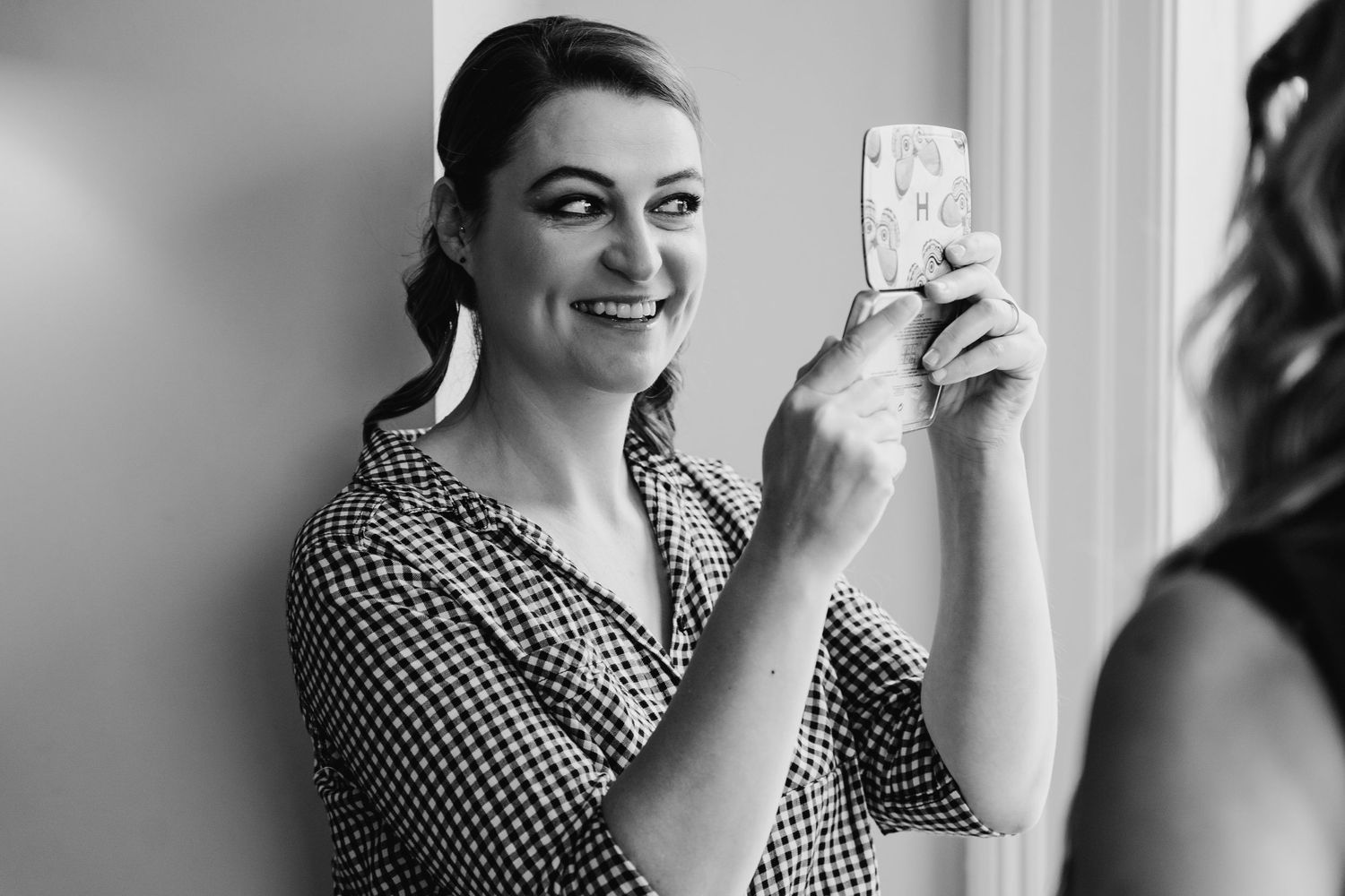 Woman in black and white checkered dress laughs while holding a small object in a bright room. House Dublin Wedding Photographer