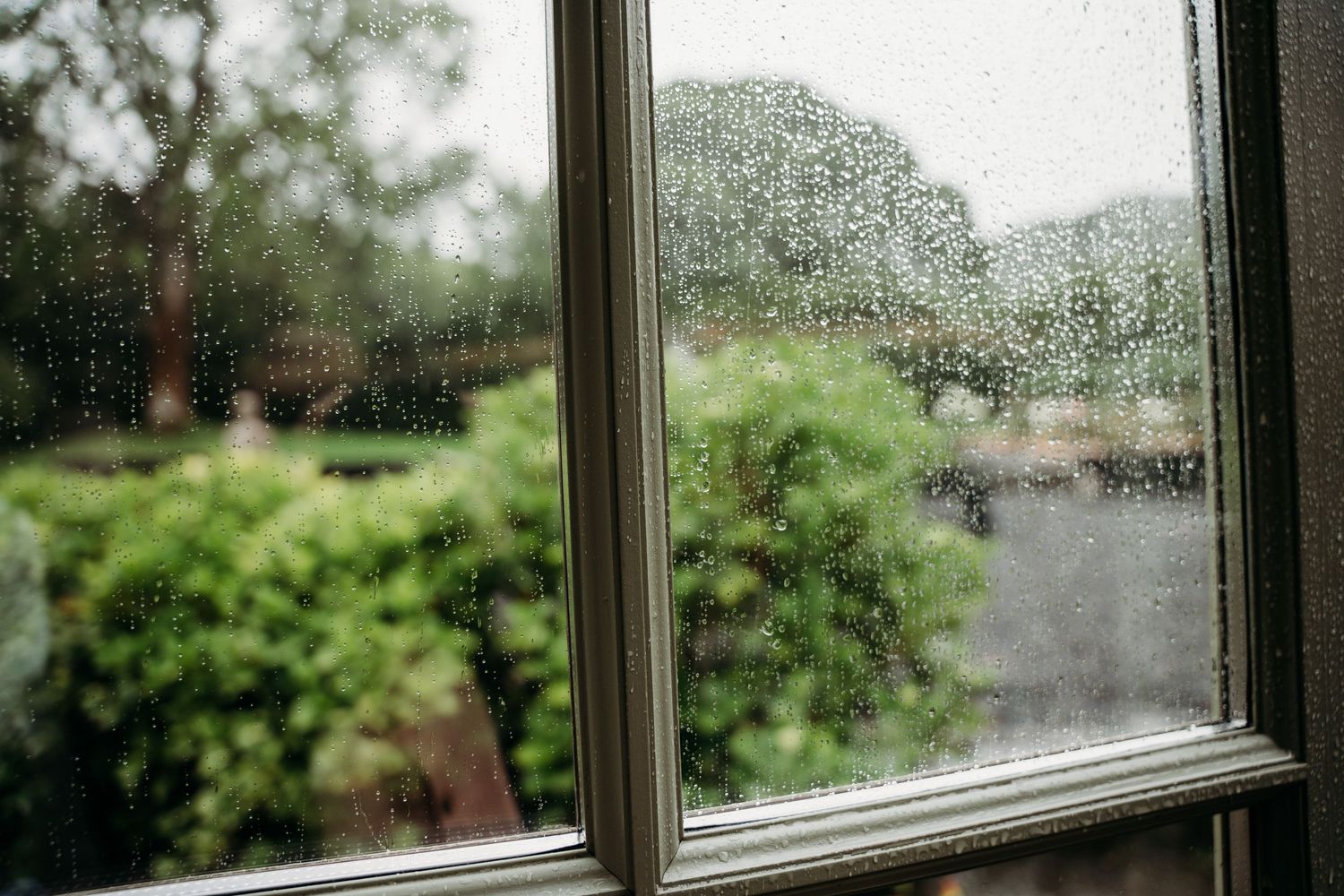 Raindrops on a window pane with blurred green garden foliage visible outside. Wedding photographer Dublin