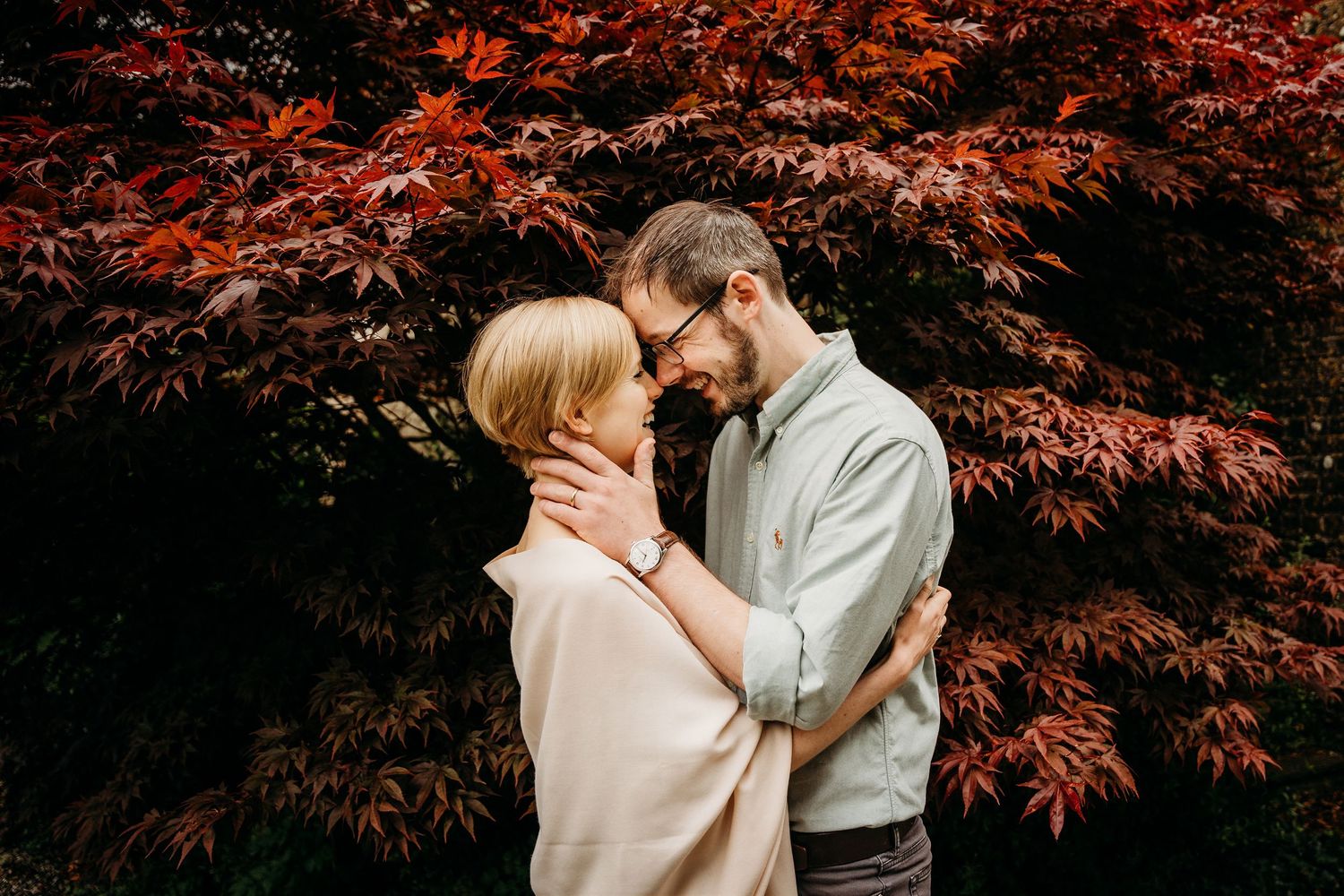 A couple shares an intimate moment in front of vibrant red Japanese maple leaves on an autumn day. PHOTOGRAPHER Dublin ireland