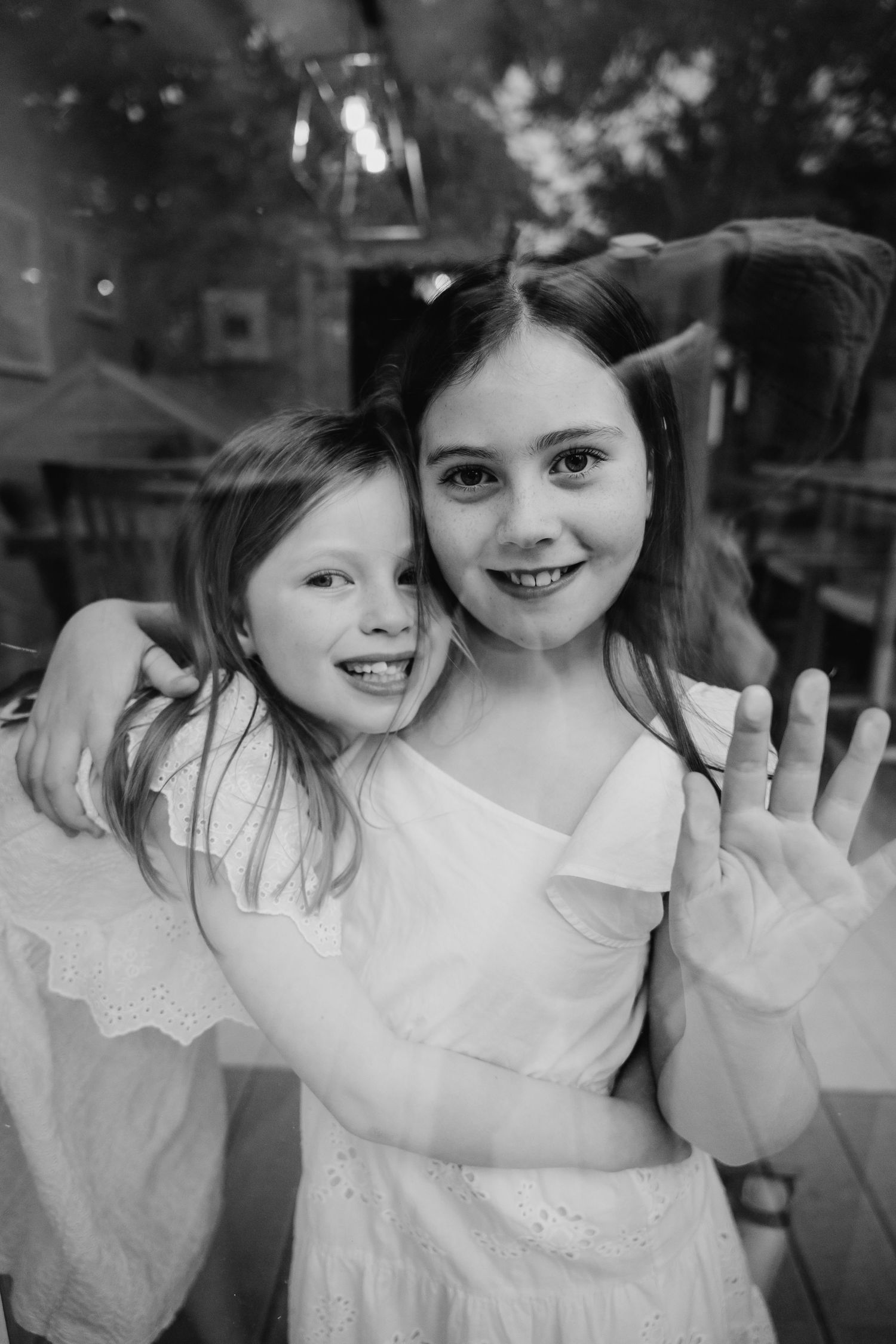 A series of black and white photos showing a child in a white dress waving and smiling through window glass. family PHOTOGRAPHER Dublin