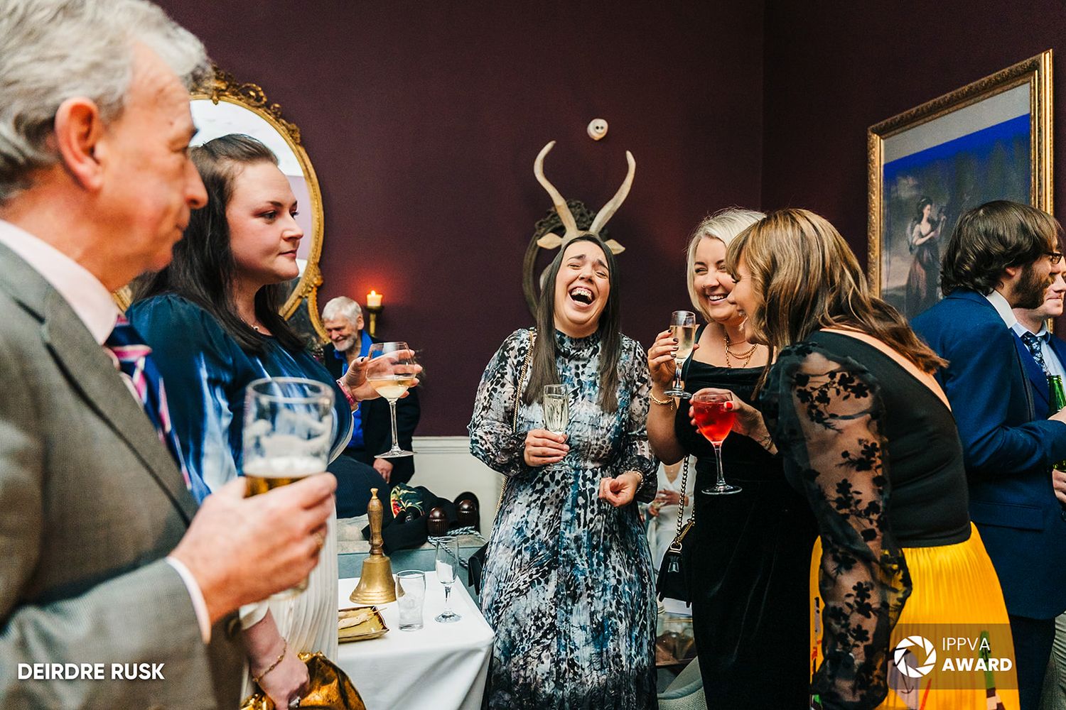 A lively party scene with people enjoying drinks and conversation at an indoor gathering. PHOTOGRAPHER Dublin Wedding PHOTOGRAPHER Dublin We