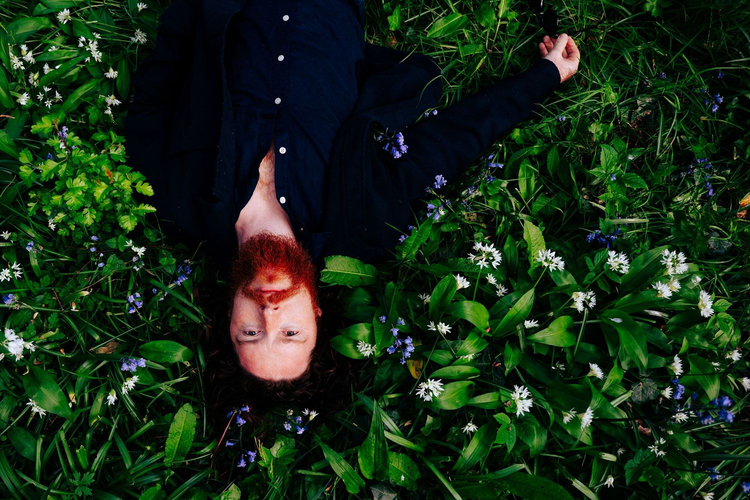A view looking down at someone lying in lush green foliage with small white flowers scattered throughout.