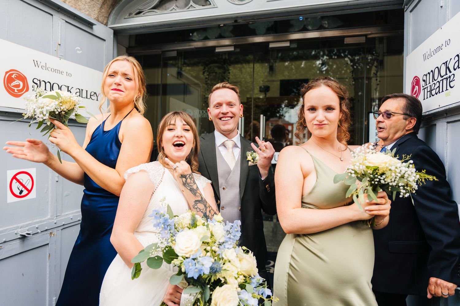 Wedding party laughing together while exiting a building with bouquets of white and blue flowers. Wedding PHOTOGRAPHER Dublin