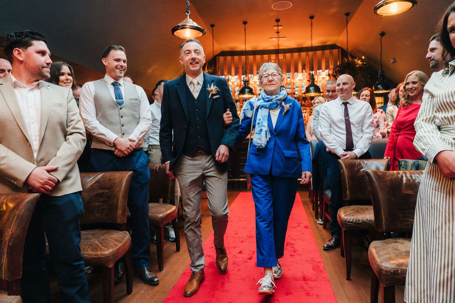 Wedding guests walking down a red carpet aisle runner in a rustic venue. Marco Pierre Dublin Wedding Photographer