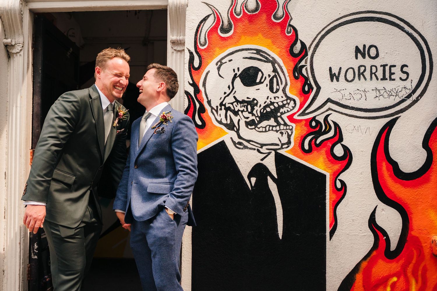 A group of people stand in front of a wall decorated with red and orange flame artwork and a skull design.