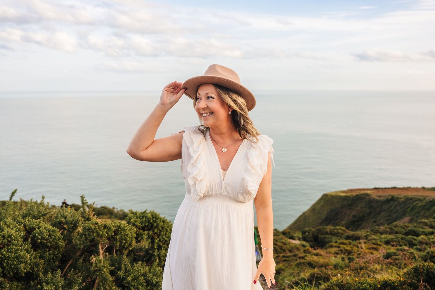 Person in white dress and brown hat exploring scenic coastal cliffs during golden hour. Professional headshots PHOTOGRAPHER Dublin