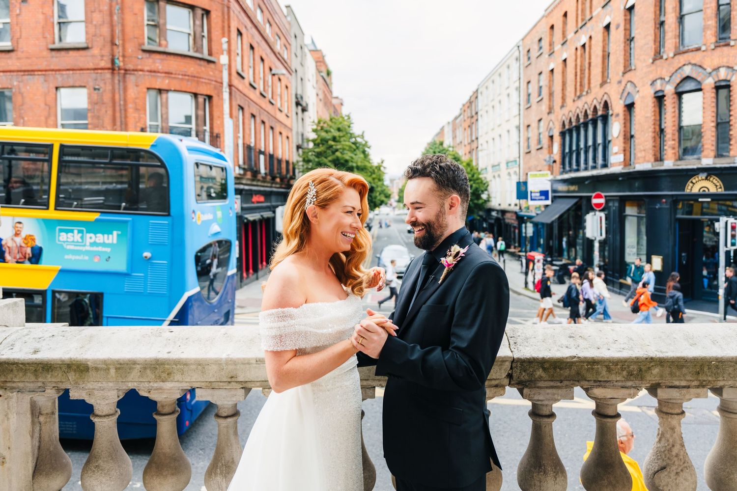 Wedding couple poses on city street with red brick buildings and blue bus in background.  city hall dublin wedding photos