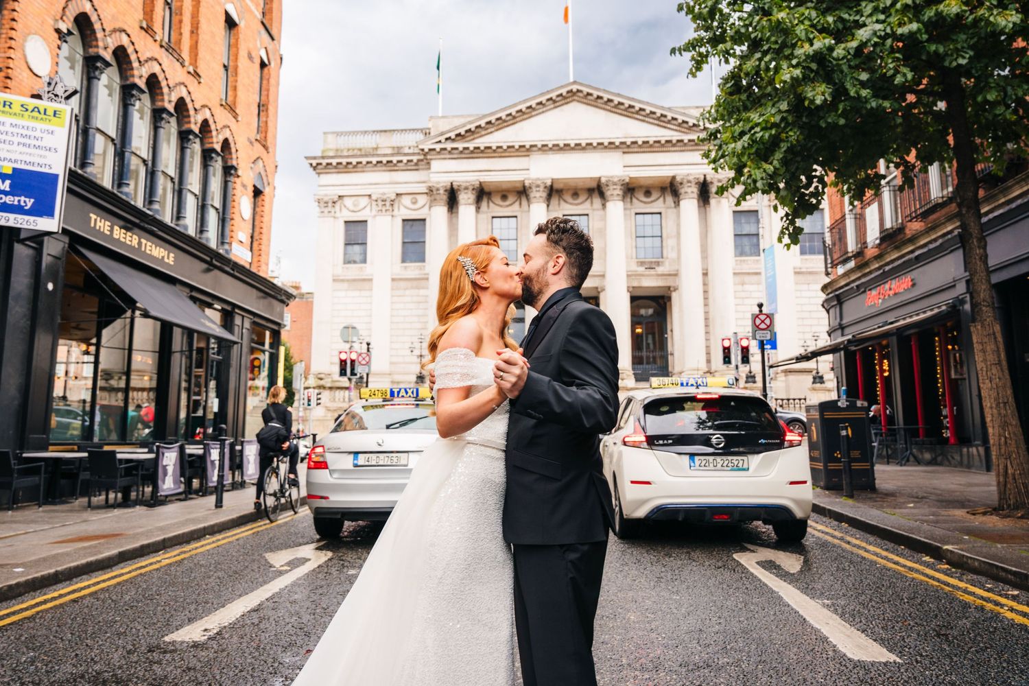 A couple poses for wedding photos on a city street with historic buildings and urban architecture in the background.  city hall dublin weddi