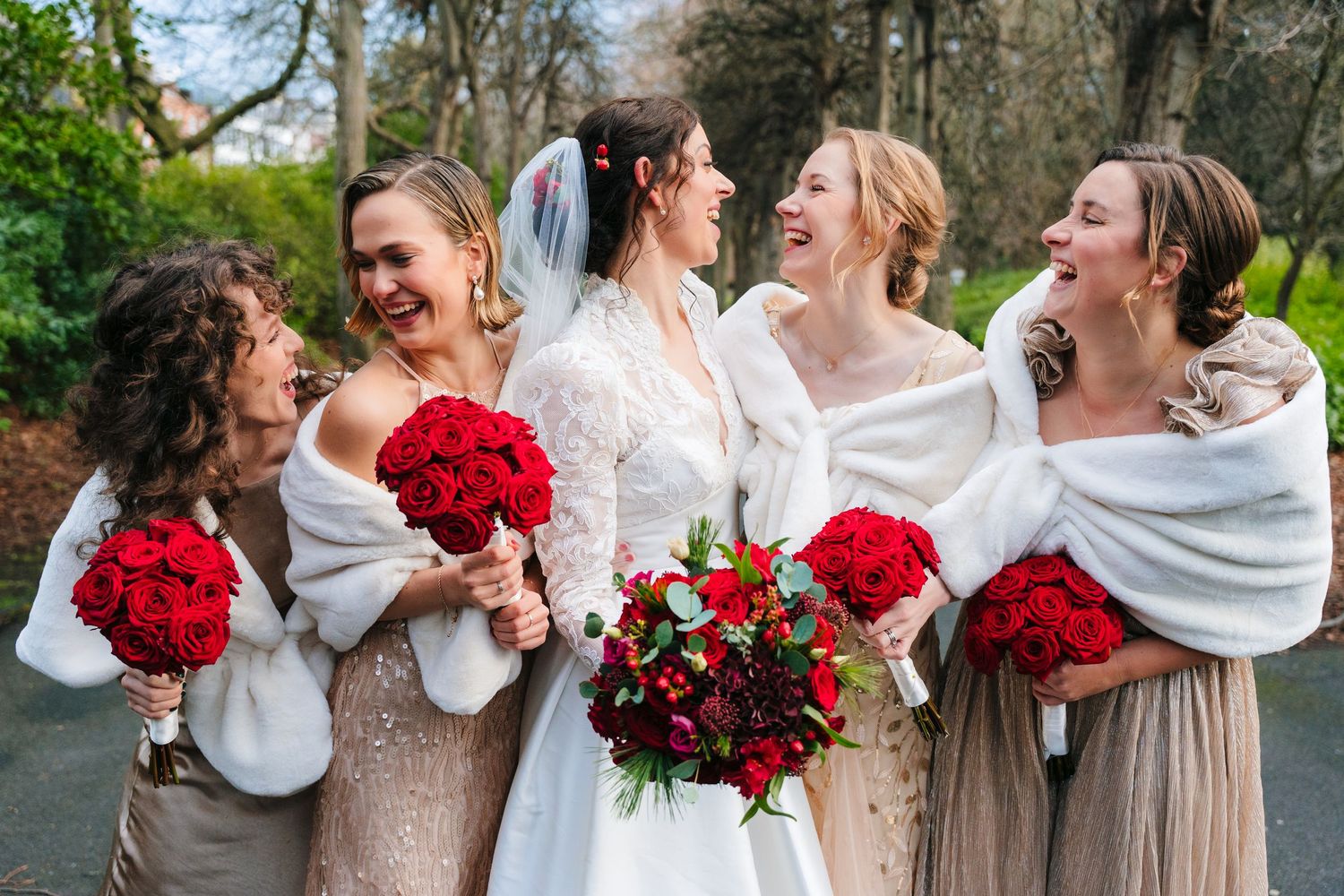 Bridal party laughing joyfully while holding red rose bouquets on a garden path. Stephens green club dublin Wedding photographer