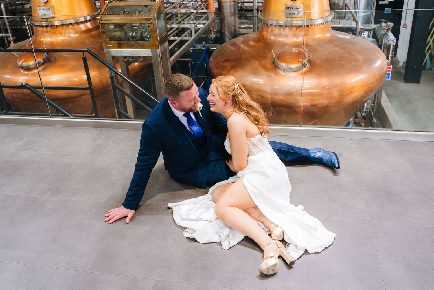 Romantic couple posing on industrial floor with copper brewing tanks in background. Dublin wedding photogrAPher