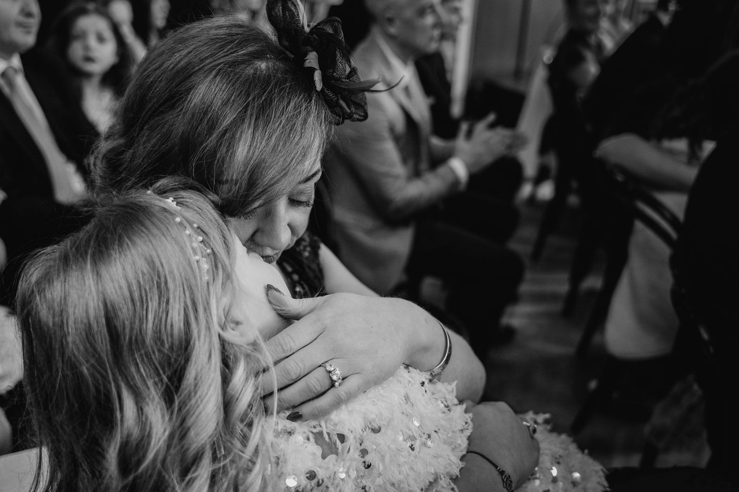Two people embrace and kiss during what appears to be a wedding celebration with guests in the background. Dublin wedding photogrAPher Bewle