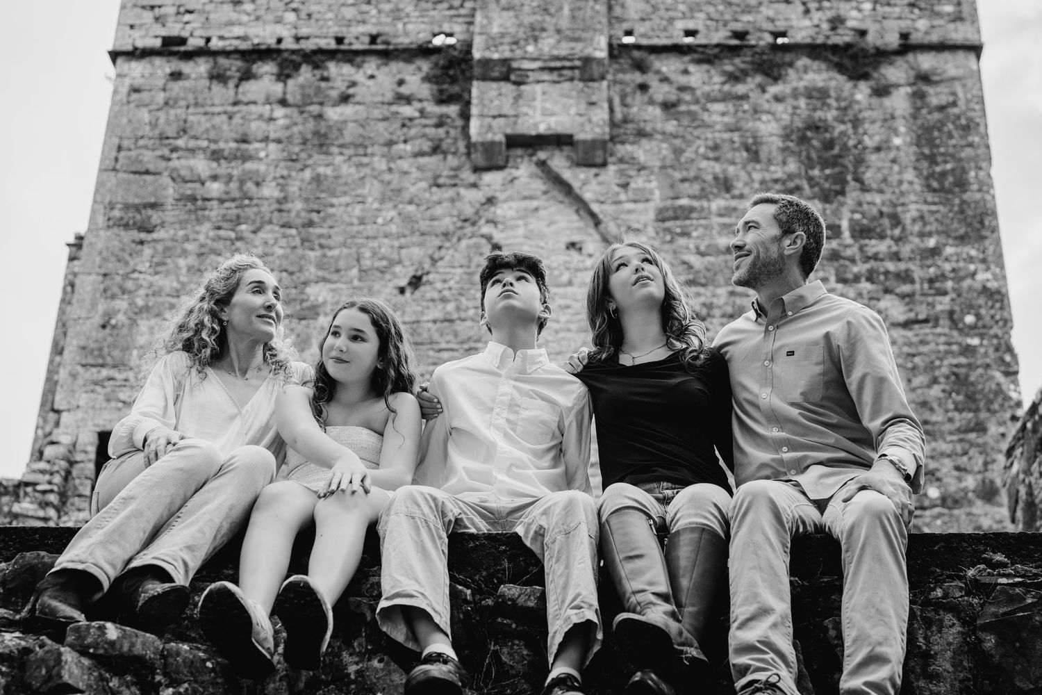Group relaxing against stone wall at historic ruins site. BEctive abbey family photographer dublin