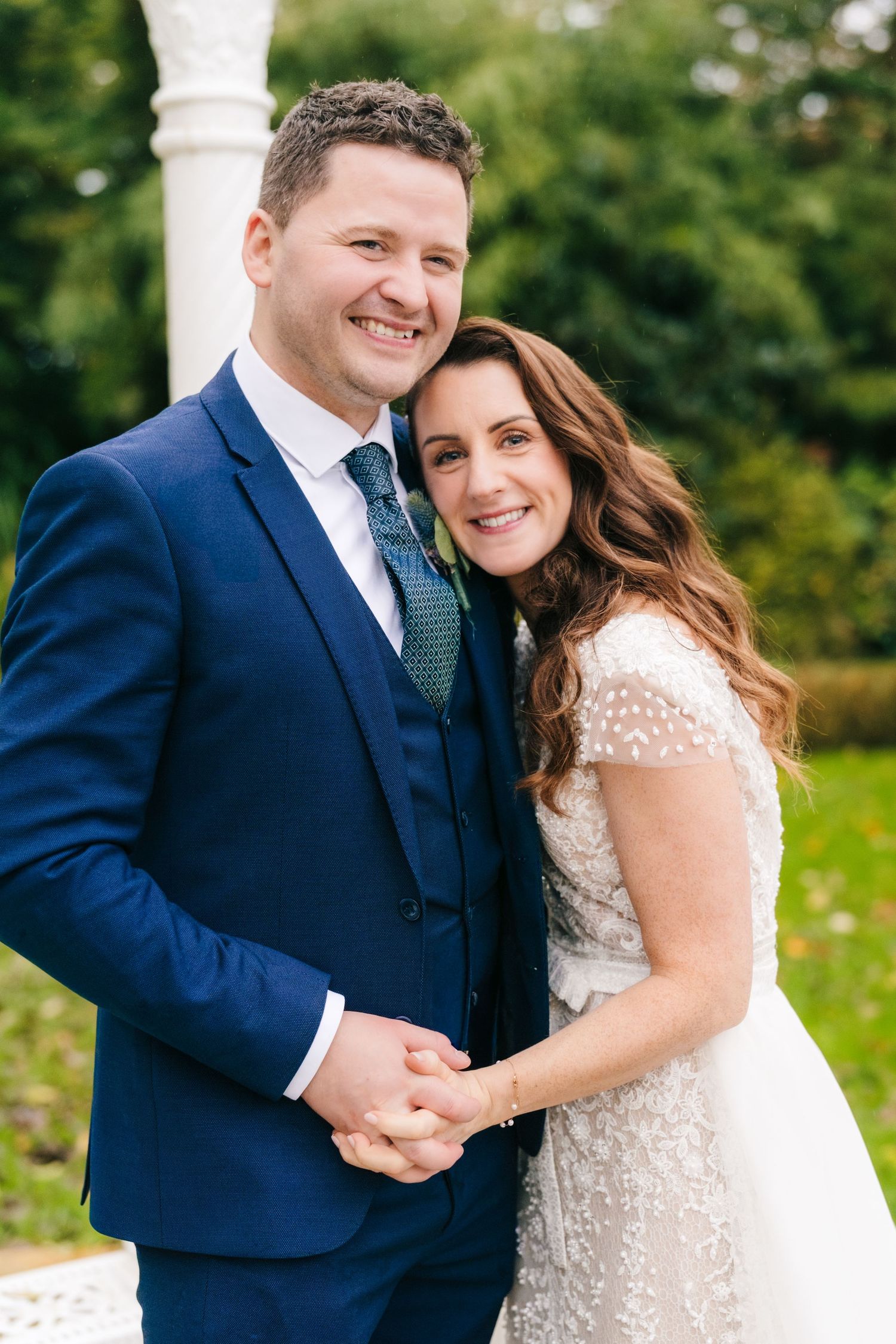 Newlyweds share a joyful moment together outdoors with greenery in the background.