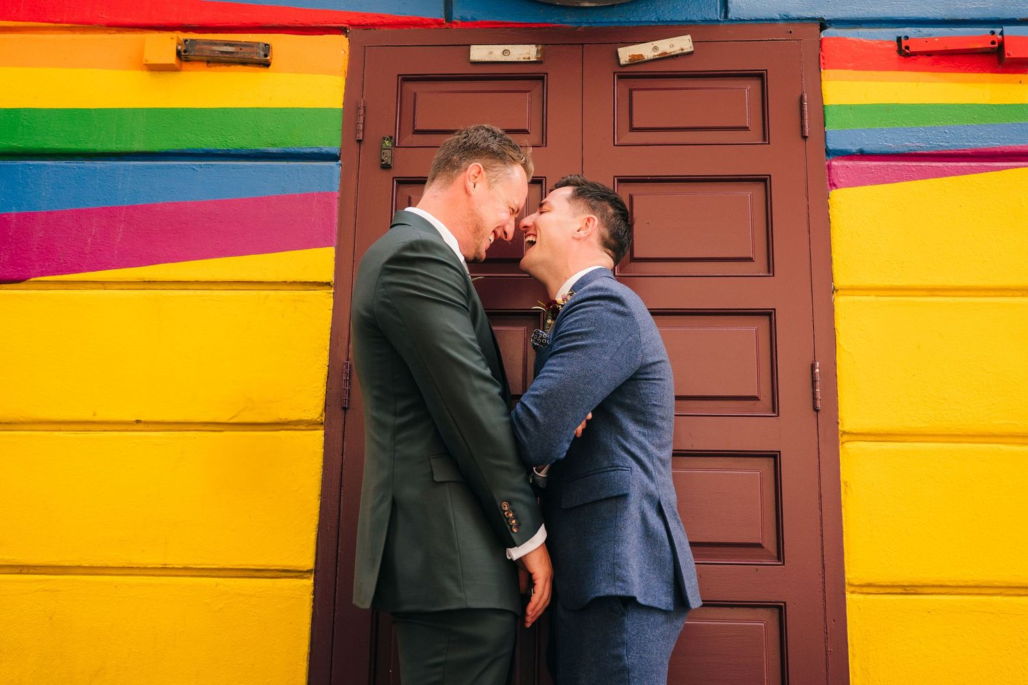 Two people share a romantic moment in front of a colorful striped wall with a brown wooden door. wedding photographer dublin pricing meath
