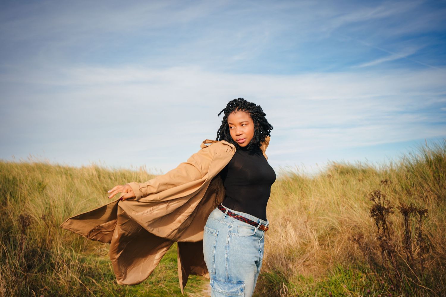 Person in tan coat and black top moving freely in coastal grassland setting. Dublin professional headshots photographer