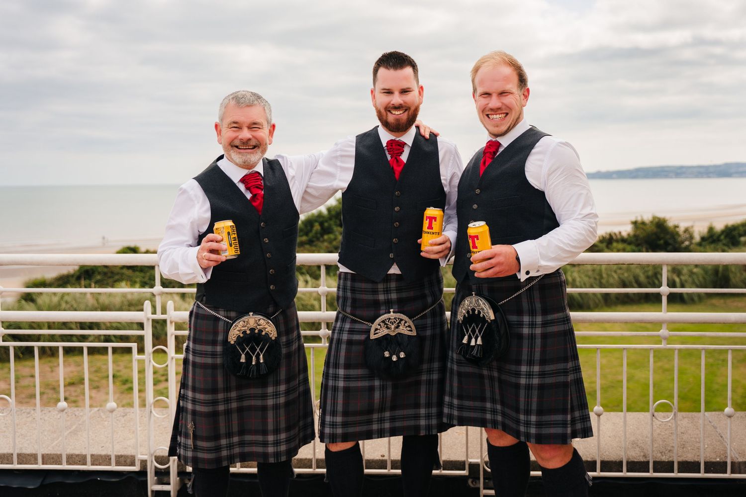 Three men in traditional Scottish kilts and sporrans hold whisky glasses while standing on a balcony overlooking the water. Portmarnock Hote