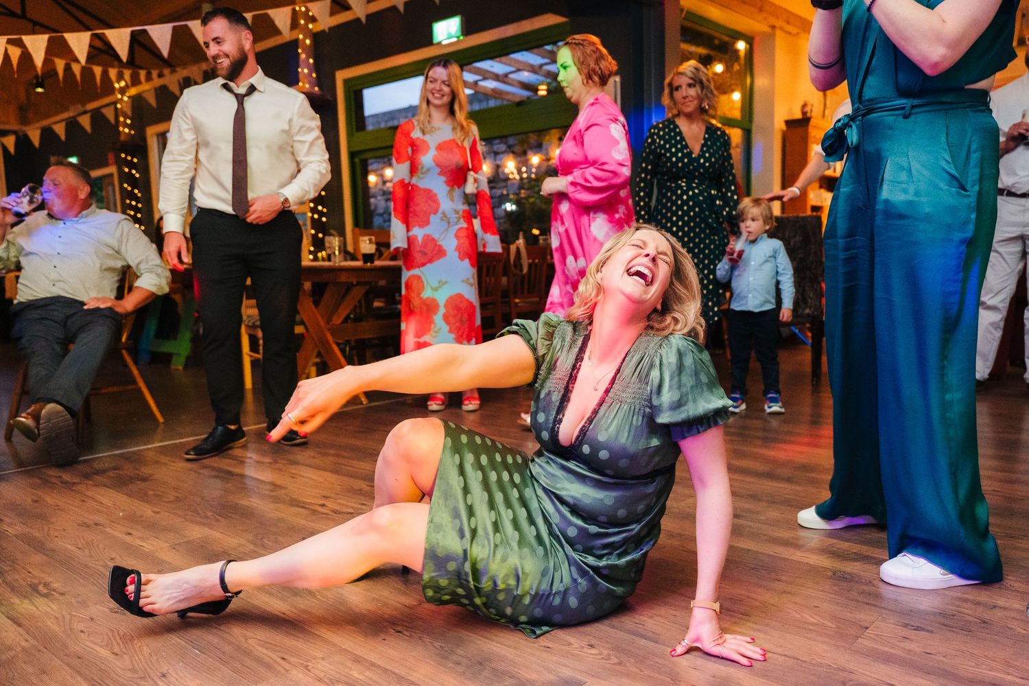 Wedding guests dancing on wooden dance floor under festive string lights and bunting. . Village Barn Tyrrellspass wedding photographer Irela