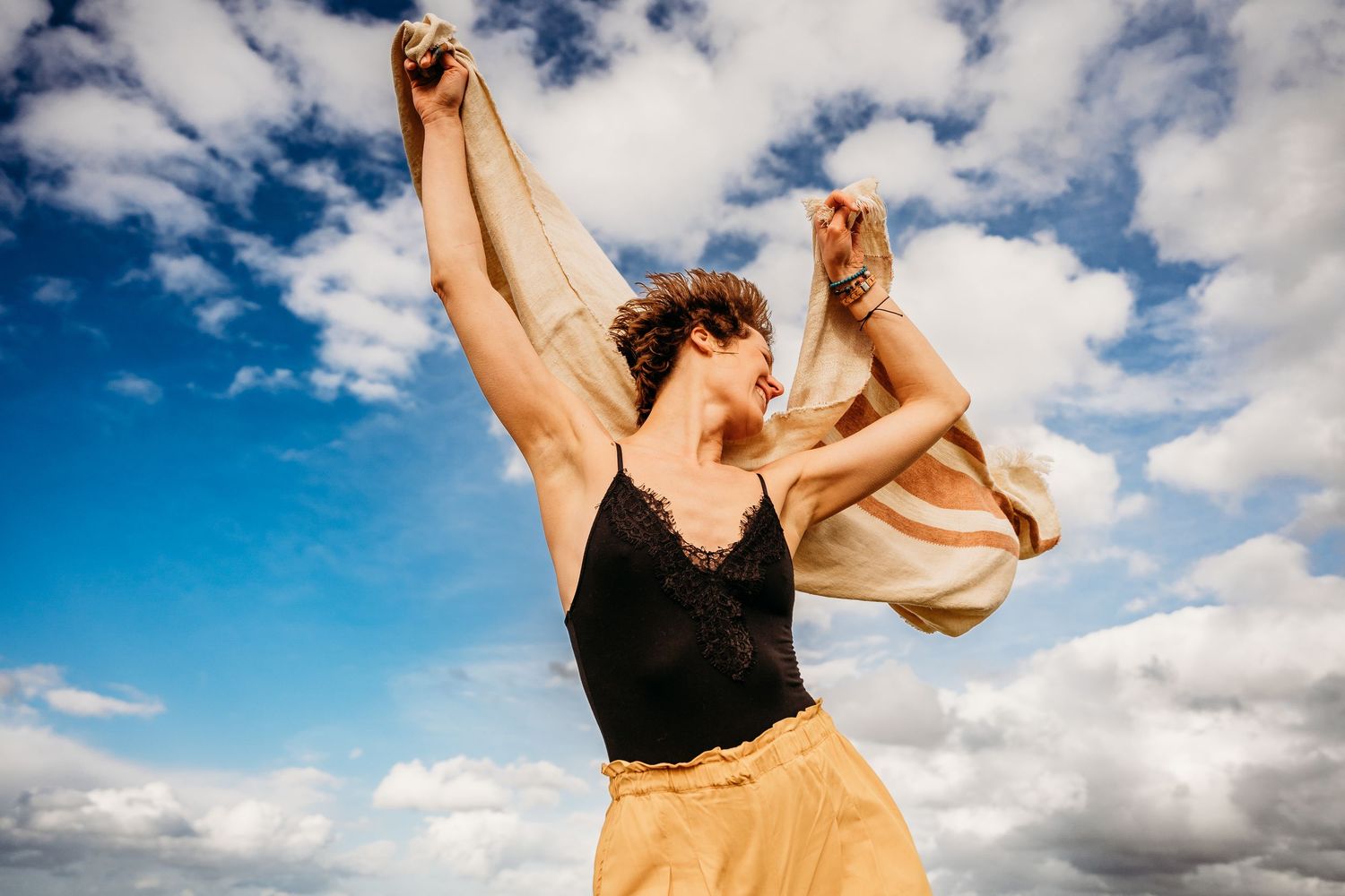 A person in black and yellow clothing dances gracefully against a dramatic blue and white cloudy sky backdrop. Portrait PHOTOGRAPHER Dublin