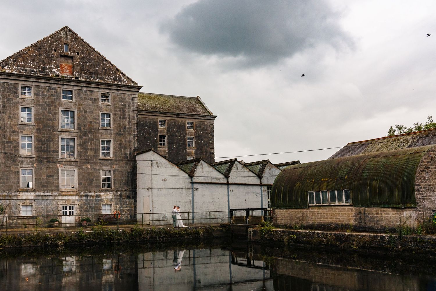 Historic brick warehouse building and storage sheds reflected in calm canal waters under cloudy skies.Millhouse slane wedding photographer d