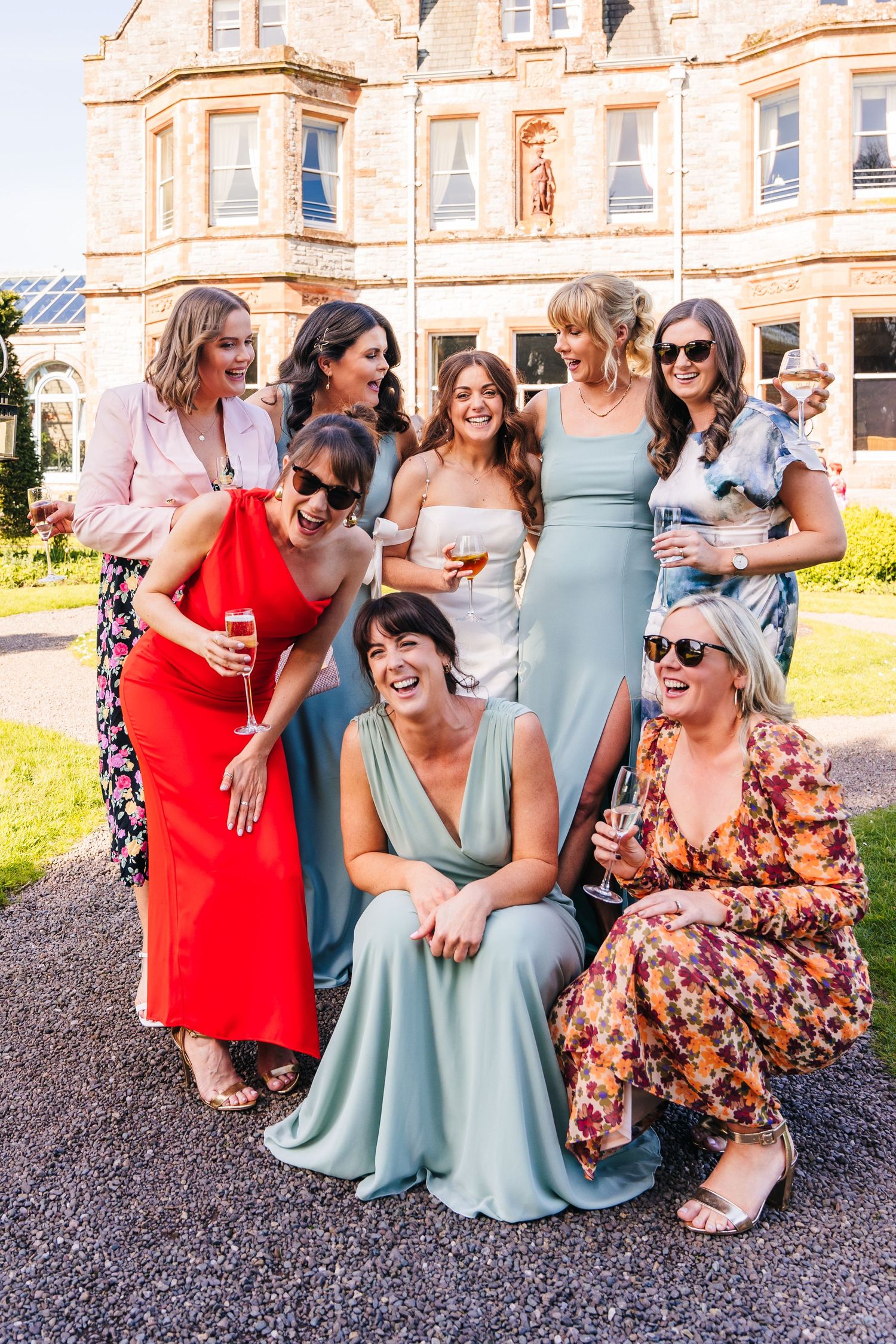 Castle Leslie Wedding Photographer Dublin Wedding party in colorful dresses poses and laughs together on the lawn of an elegant estate.