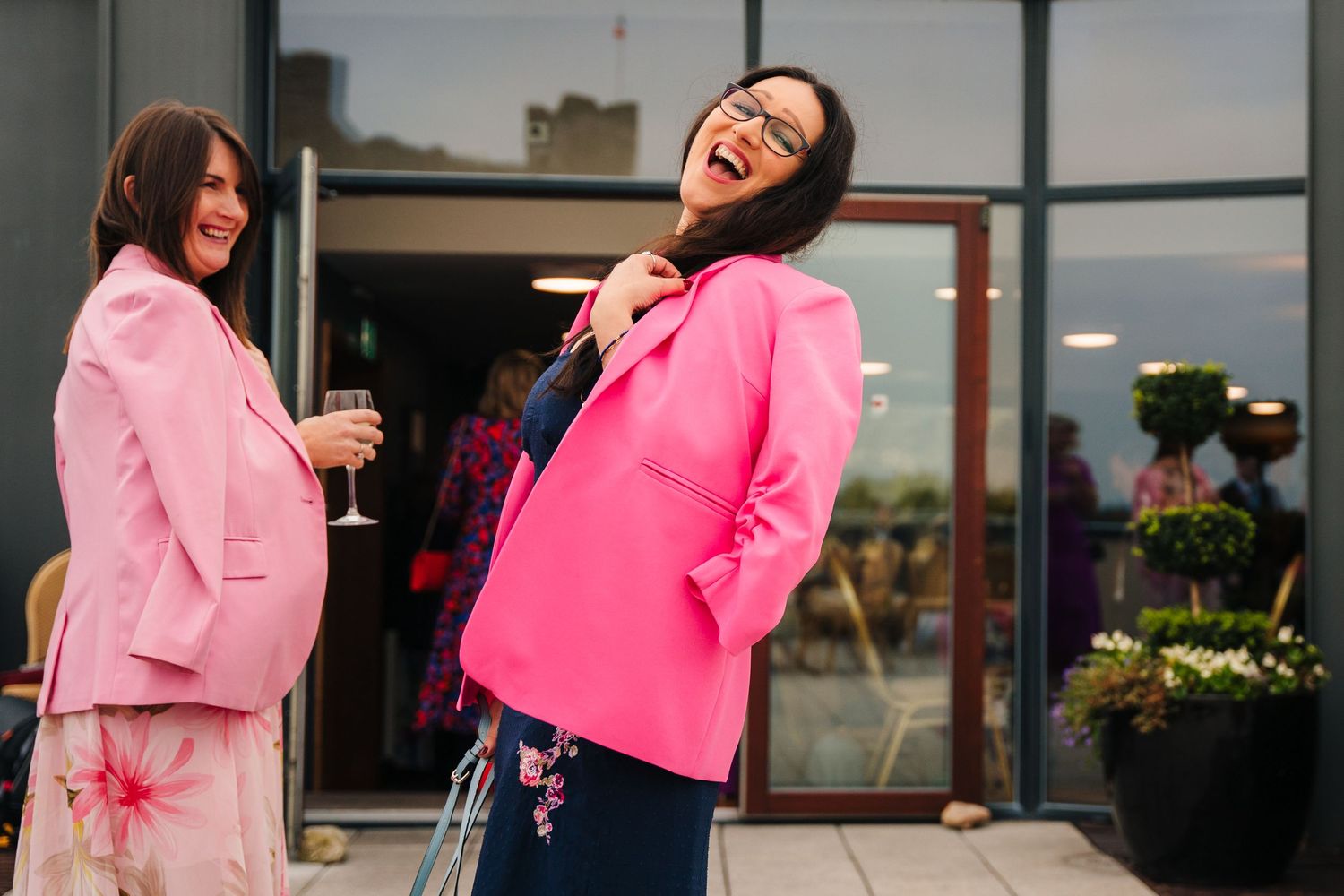 Friends in matching pink blazers share laughs at an outdoor gathering.Wedding Photography Trim Castle Ireland\