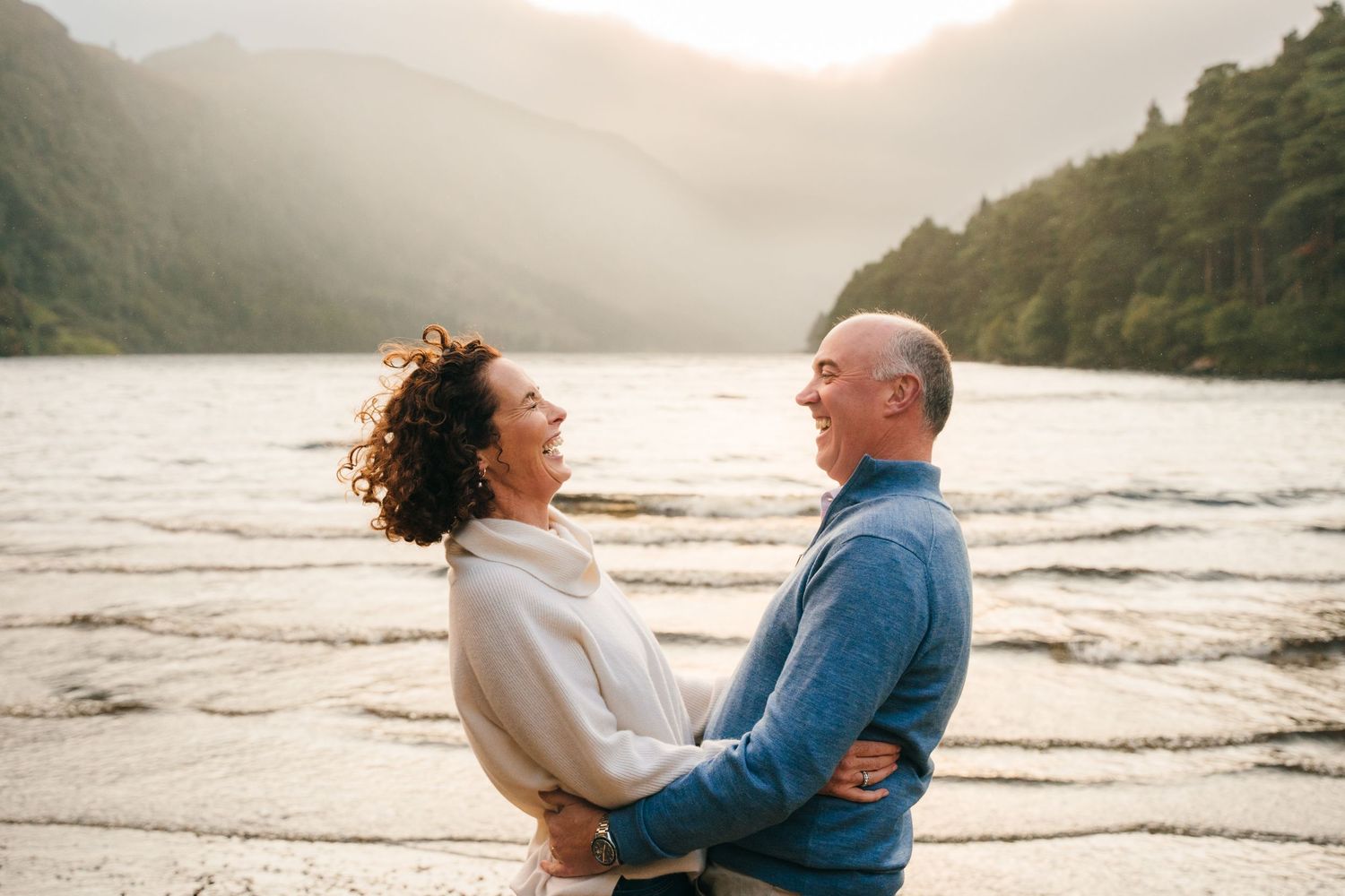 Family photographer Ireland Dublin A romantic sunset moment by a serene lake surrounded by misty mountains.