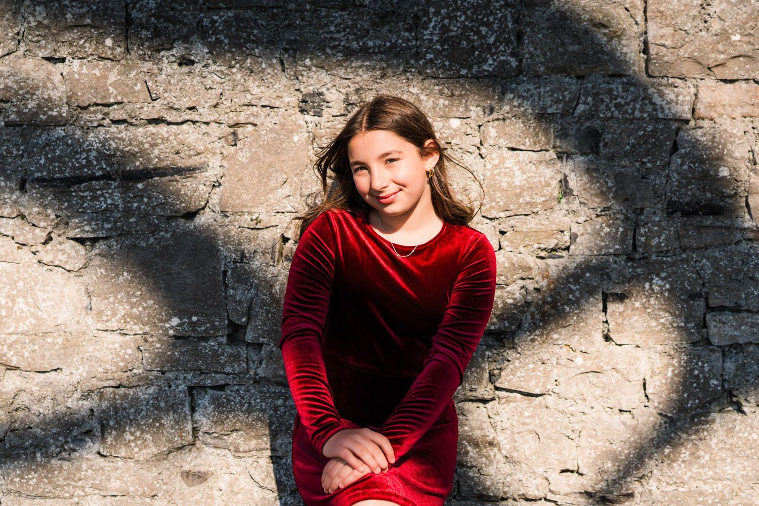 A velvet red dress stands out against a textured stone wall with dramatic shadows. Family PHOTOGRAPHER Dublin