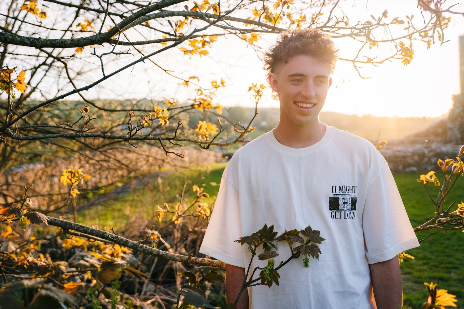Person wearing a white t-shirt standing under autumn tree branches at sunset. Photographer Ireland dublin
