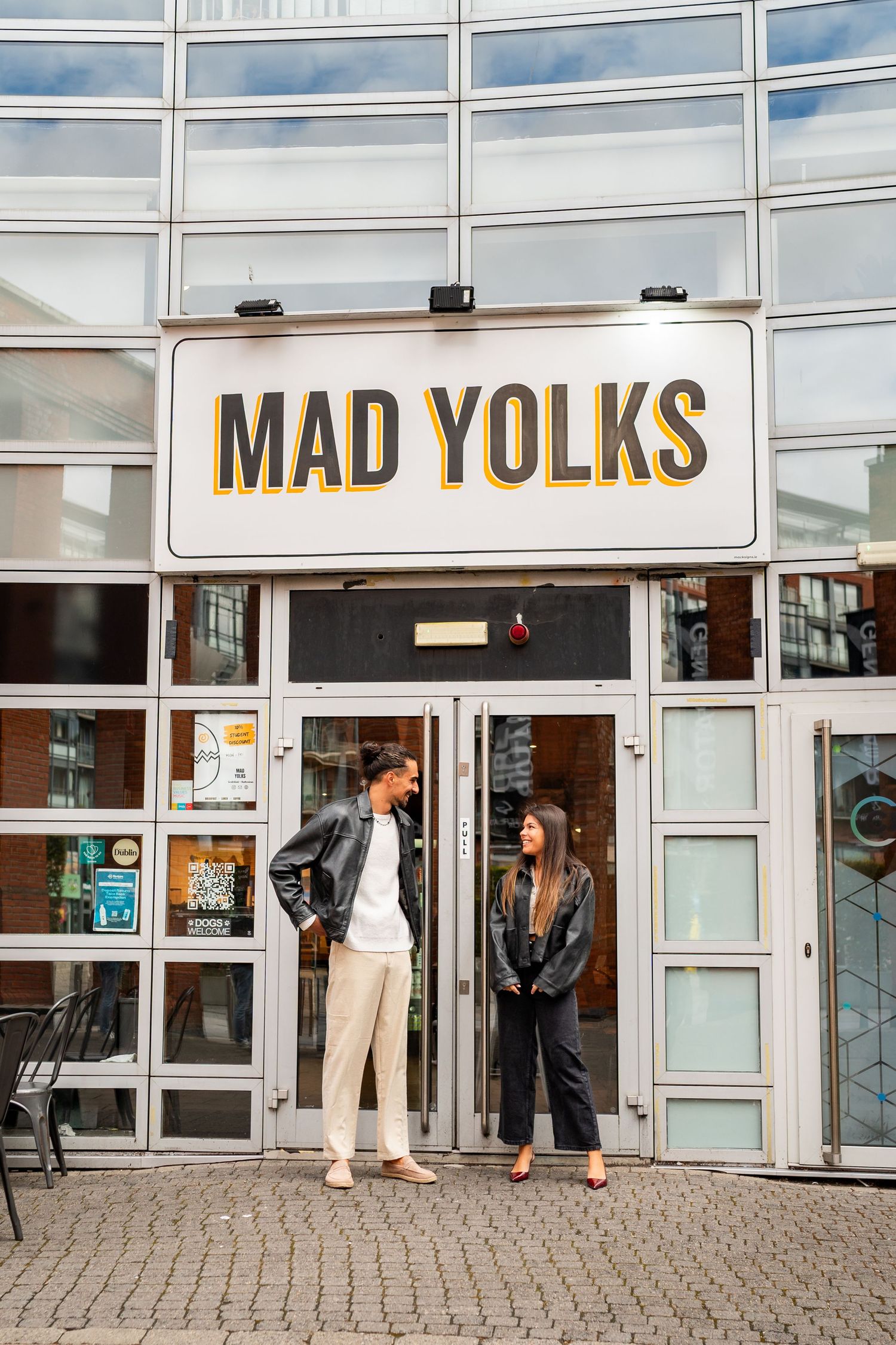 A couple stands outside the Mad Yolks storefront with large glass windows and signage. Couple's Photoshoot PHOTOGRAPHER Dublin