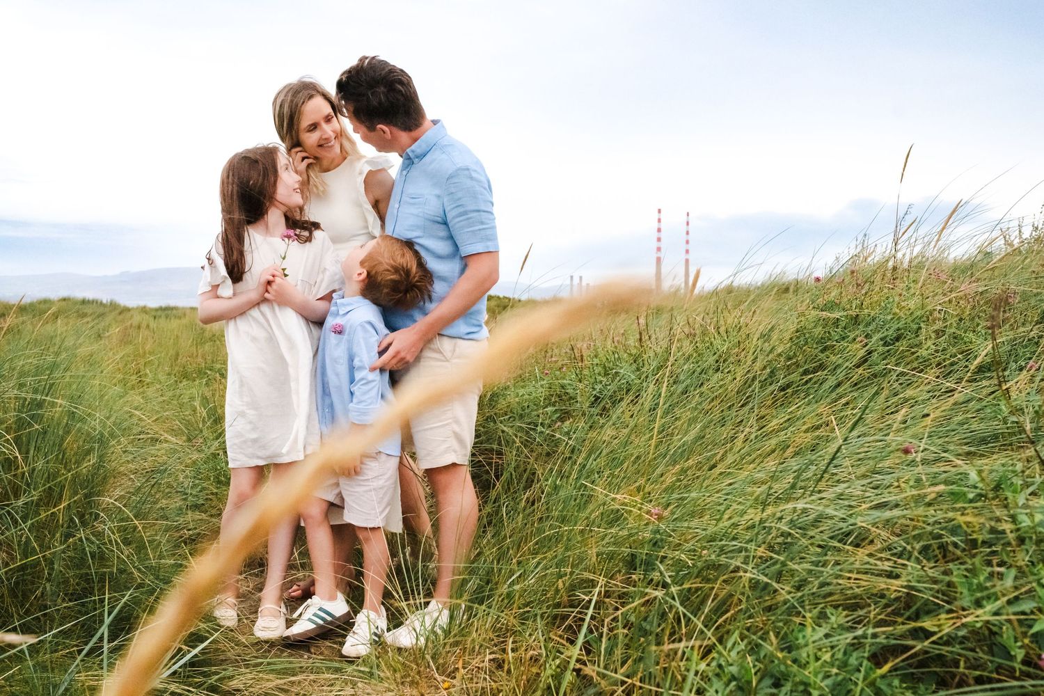 A relaxed family photoshoot among windswept coastal grass on a sunny day.  Family photographer Dublin Ireland