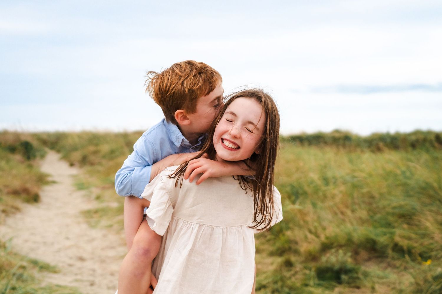 Two people share a joyful moment together on a grassy trail beneath cloudy skies.  Family photographer Dublin Ireland