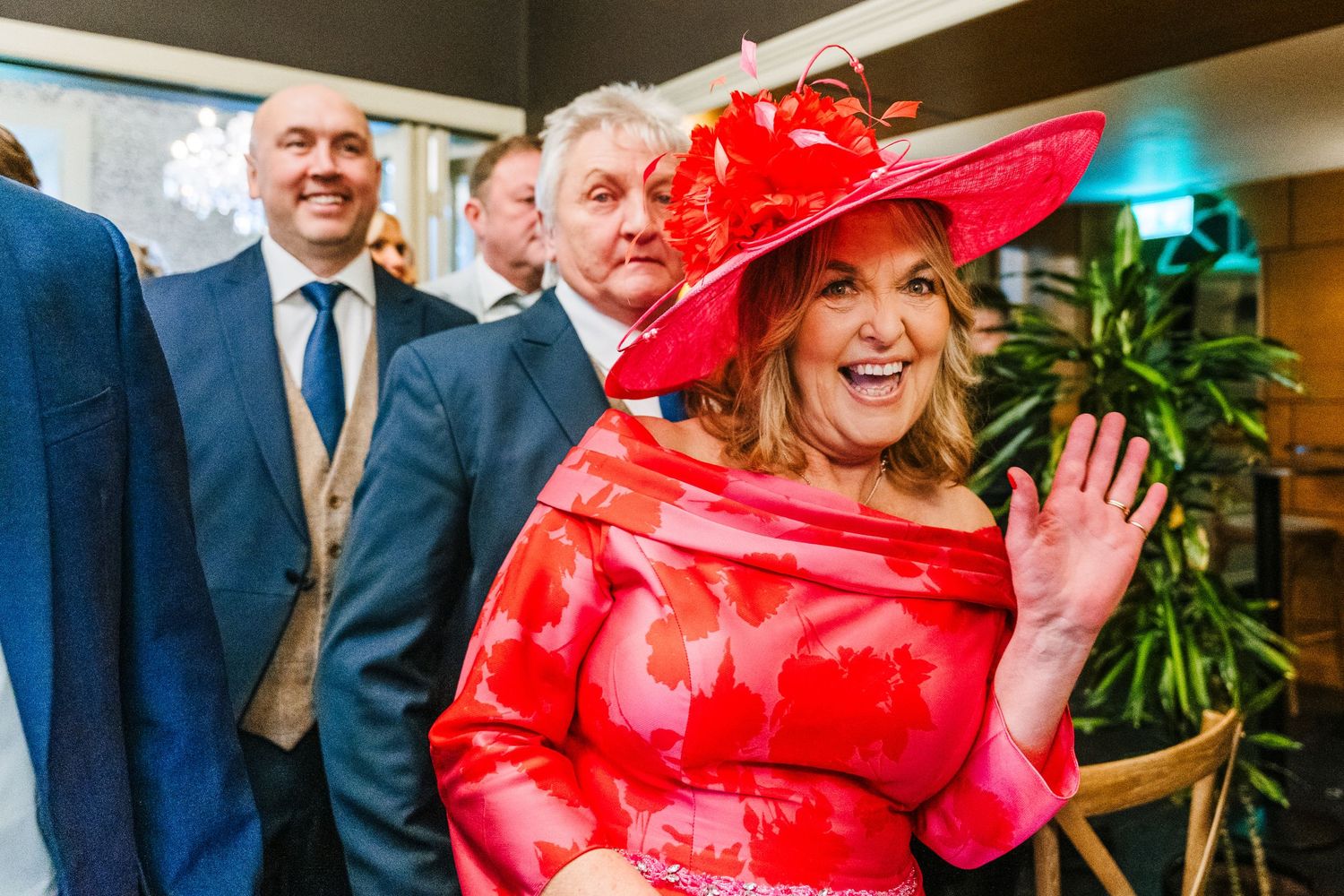 A woman in a bright pink hat and dress shares a joyful moment at an elegant celebration.  Virginia Park Lodge Wedding Photographer Cavan Dub