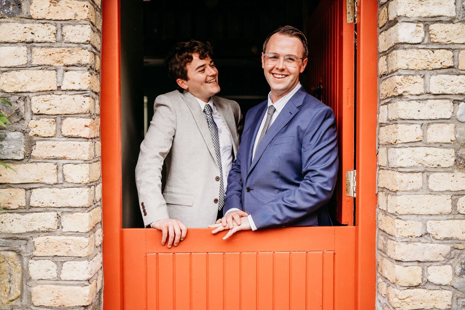 A couple shares joyful moments through red-framed windows of a rustic stone building. Wedding photographer Dublin